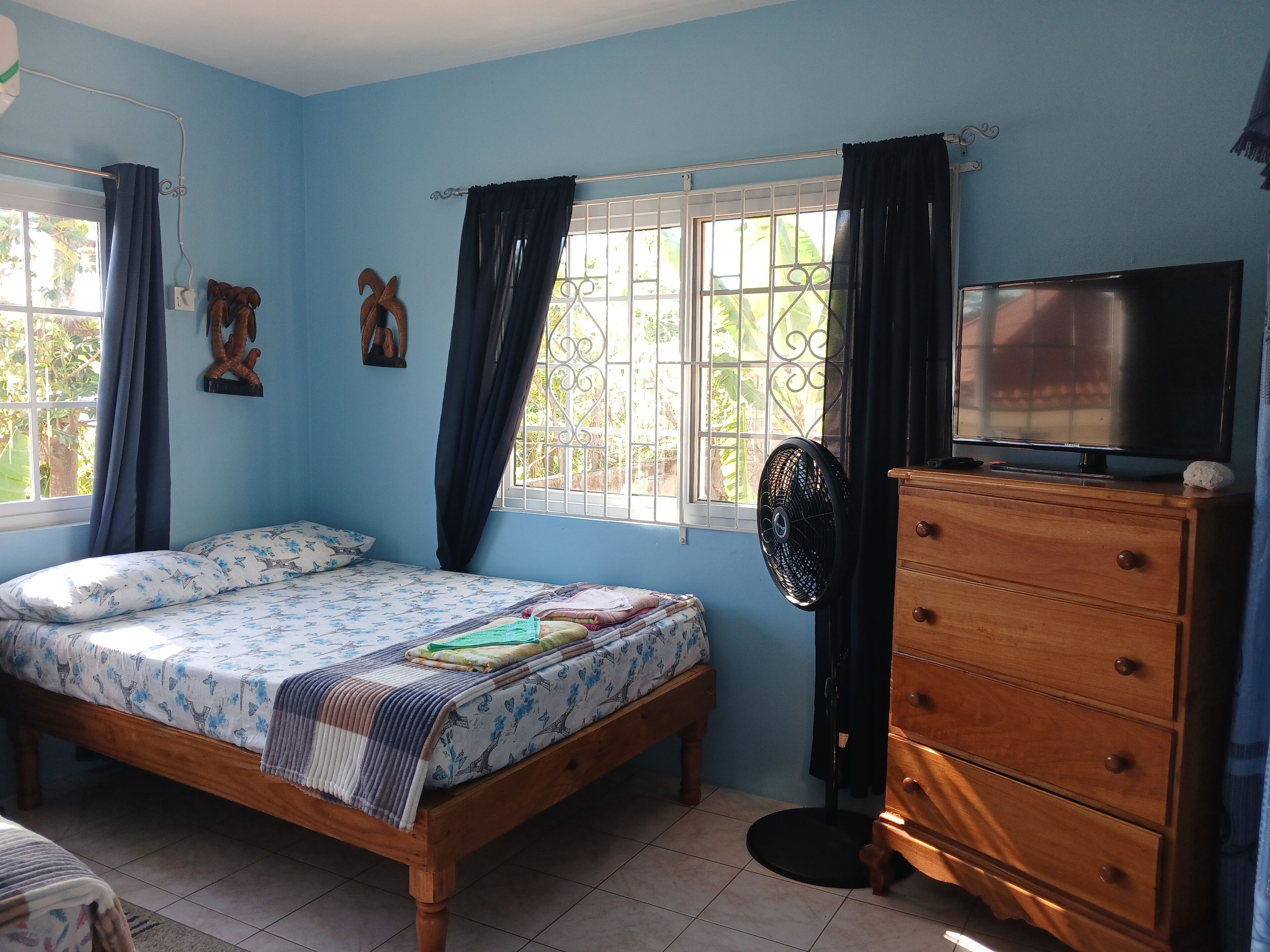 A bedroom with a bed, wooden dresser, TV, and a window with curtains.