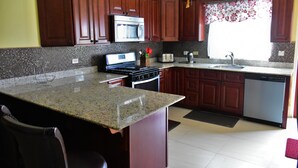 A kitchen with wooden cabinets, a granite countertop, a microwave, a stove, a sink, and a dishwasher. - Plantation Villa 354 - Ocho Rios (St. Ann's Bay)