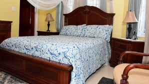 A bedroom with a wooden bed, a nightstand, a lamp, and a chair. - Plantation Villa 354 - Ocho Rios (St. Ann's Bay)