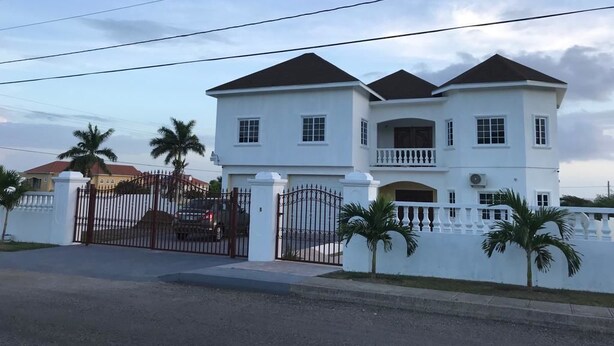 A large, two-story white building with a symmetrical facade, a gated entrance, and a small balcony on the second floor. - Plantation Villa 354 - Ocho Rios (St. Ann's Bay)