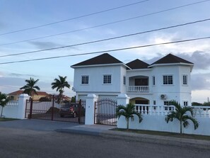 A large, two-story white building with a symmetrical facade, a gated entrance, and a small balcony on the second floor. - Plantation Villa 354 - Ocho Rios (St. Ann's Bay)