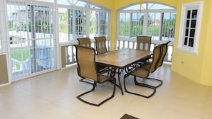 A dining area with a large table and chairs, large windows with white frames, and a ceiling fan. - Plantation Villa 354 - Ocho Rios (St. Ann's Bay)