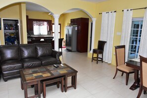 A living room with a leather sofa, a coffee table, and a dining area with a wooden table and chairs.