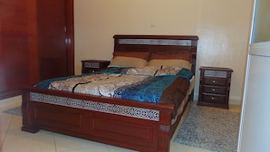 A wooden bed with intricate carvings, a matching nightstand, and a small drawer unit. - Suite Apartment Fawzi (Agadir)