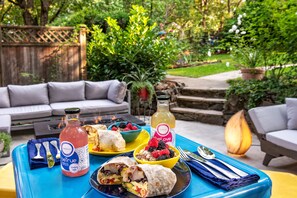 A patio with a blue table set with food, drinks, and a bottle of Bel-True. - Inn at the Gorge (Hood River)