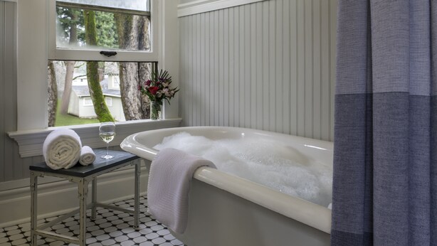 A bathroom with a bathtub, a window with a view of trees, and a tiled floor. - Inn at the Gorge (Hood River)