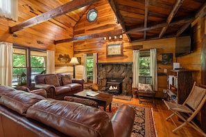 A cozy log cabin interior with leather sofas, a stone fireplace, and wooden beams. - Butterfly Hollow B&B (Gordonsville)