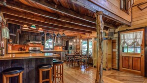 Una cocina rústica con pisos de madera, una barra con taburetes y un gran poste de madera.
