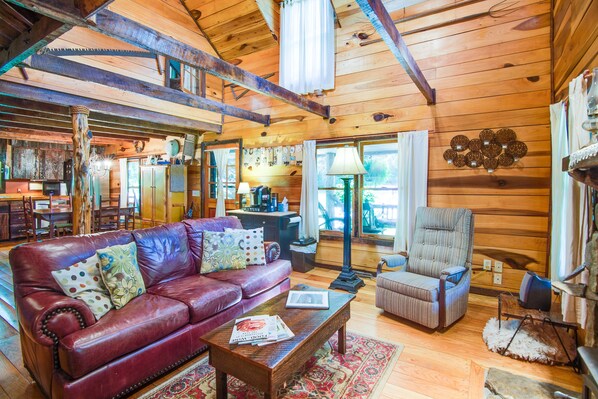 A cozy cabin interior with a wooden ceiling, a leather sofa, a striped armchair, and a dining area with a wooden table and chairs. - Butterfly Hollow B&B (Gordonsville)