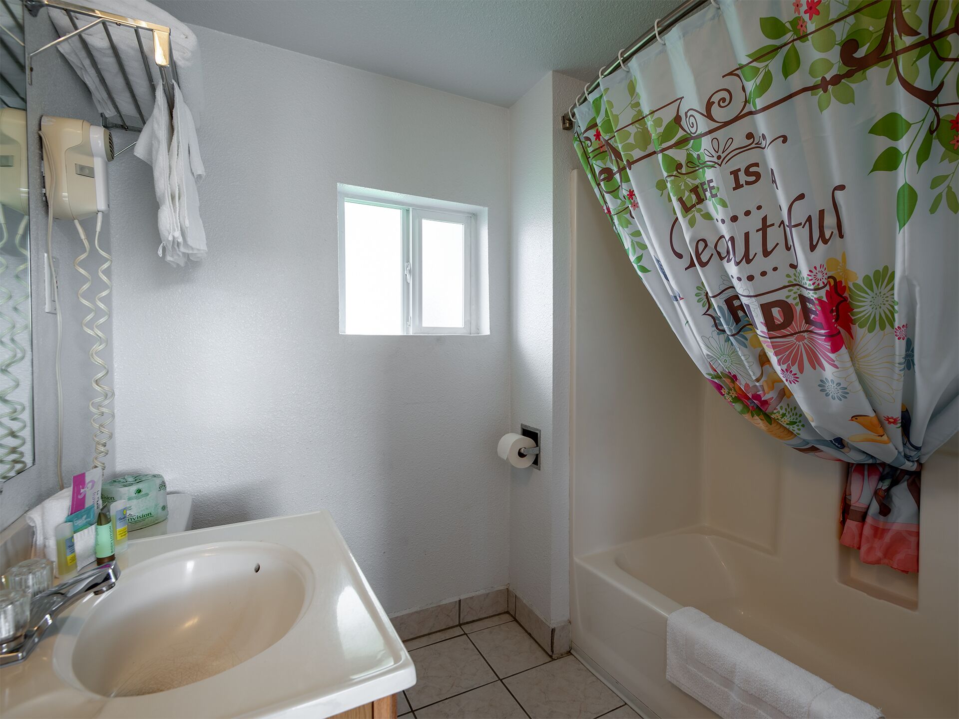 A bathroom with a white sink, a window, a shower curtain with floral patterns, and a towel rack.