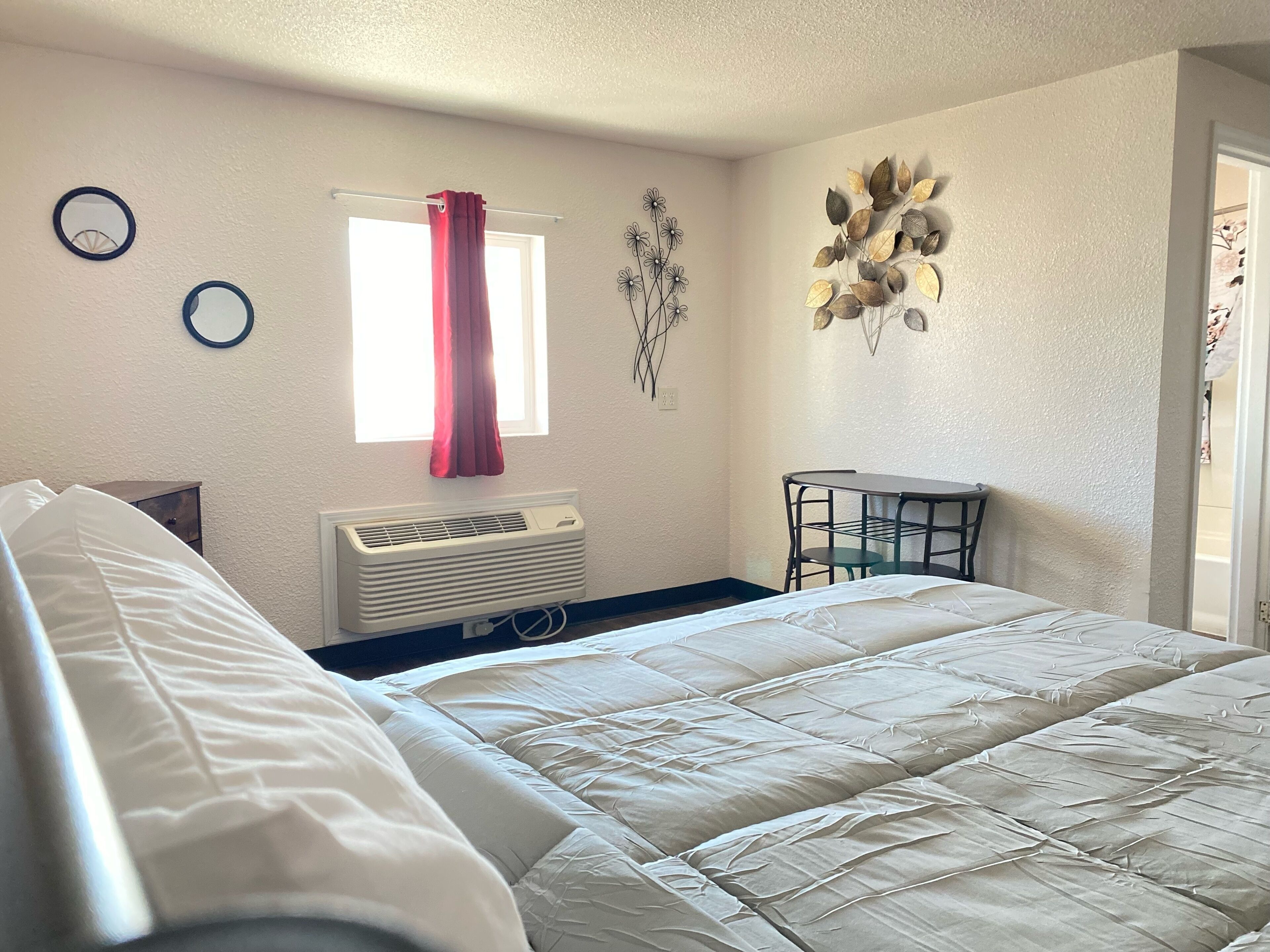 Un dormitorio con cama, ventana con cortina, radiador, una mesita y adornos en la pared.