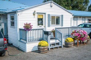 A white building with a blue roof, a porch with a railing, and flower pots on the front. - Baker City Motel & RV Park (Baker City)