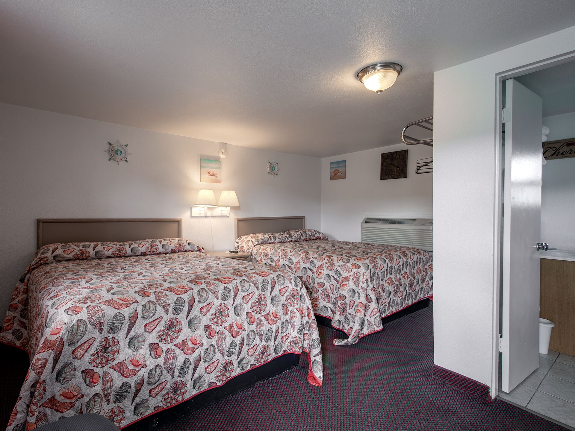 A hotel room with two beds, a bathroom, and a hallway.