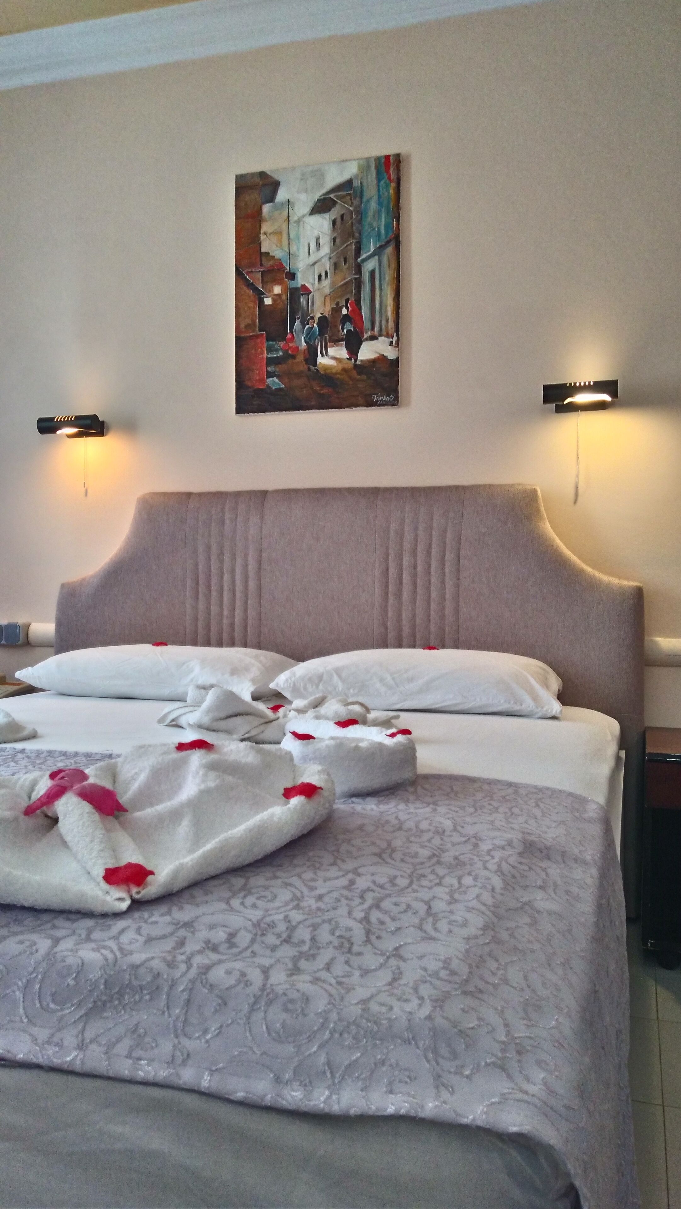 A hotel room with a large bed, two wall-mounted lights, and a painting of a street scene.