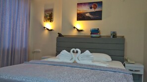 Una camera d'albergo con un letto decorato con un cigno fatto di asciugamani, una lampada da comodino, un comodino con un telefono e opere d'arte alle pareti raffiguranti un tramonto e mongolfiere.