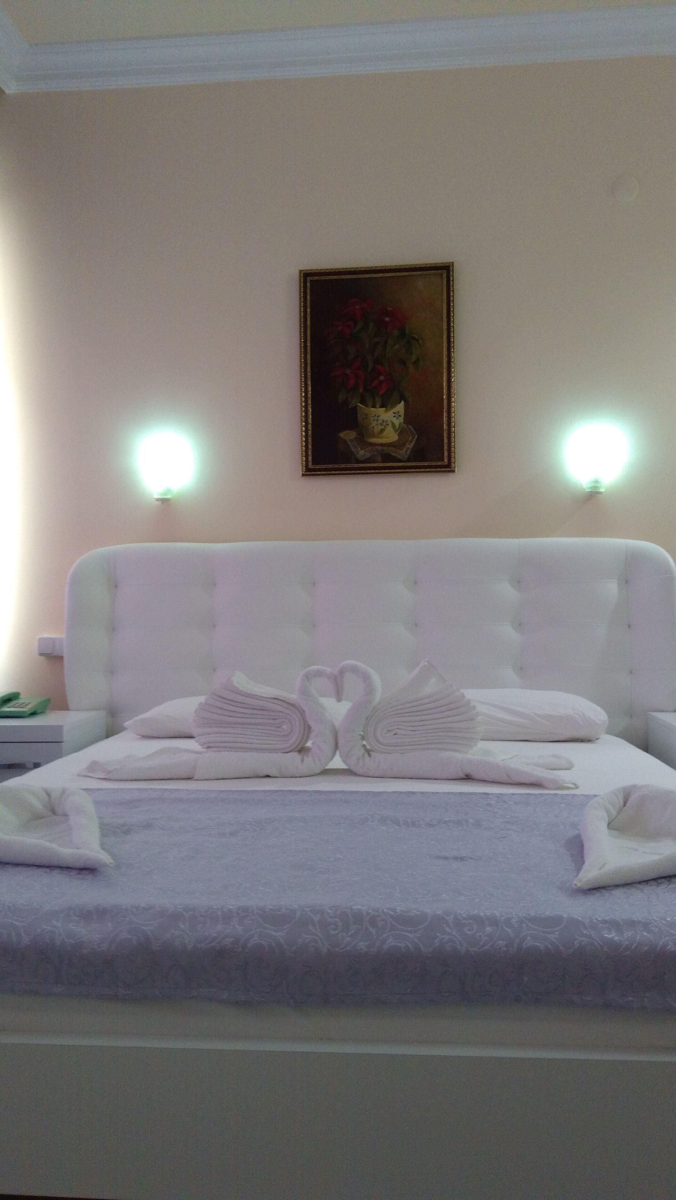 Una camera d'albergo con un letto grande, un quadro appeso al muro e due lampade a parete.