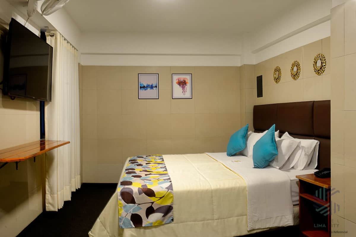A hotel room with a bed, a TV mounted on the wall, and a small table.