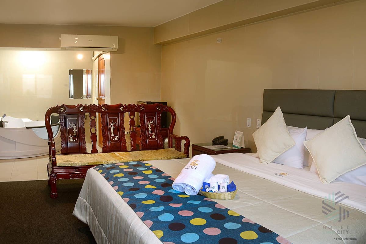 A hotel room with a bed, a wooden bench, a small table, a telephone, and a mirror.