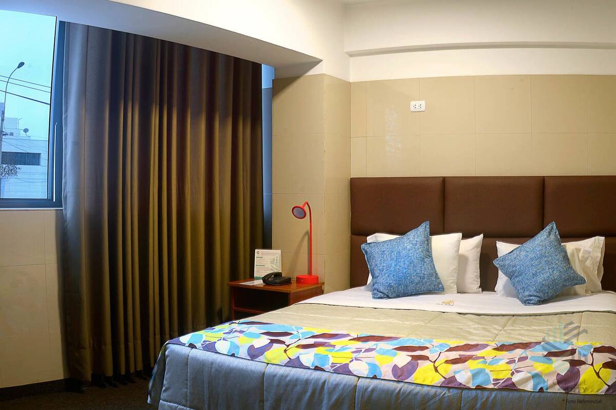 A hotel room with a large bed, a nightstand, a telephone, and a window with curtains.