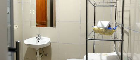 A bathroom with a white sink, a mirror, a toilet, and a metal shelf with towels.