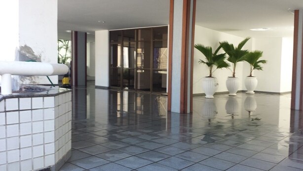 A spacious lobby with a tiled floor, large potted plants, and a glass partition. - Ed. Bosque das Azaleias (Salvador)
