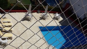 A chain-link fence surrounding a pool area with lounge chairs and umbrellas. - Ed. Bosque das Azaleias (Salvador)