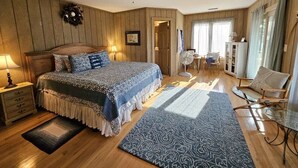 A bedroom with a bed, a nightstand, a fan, a chair, and a window with curtains.