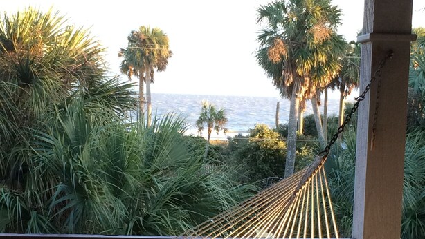 A hammock on a wooden deck with a view of the ocean and palm trees.