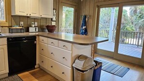 A kitchen with white cabinets, a dishwasher, a trash can, and a view of a balcony with outdoor furniture.