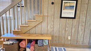 A wooden staircase with a bench at the bottom, wicker baskets with towels, and a framed picture of a beach scene on the wall.