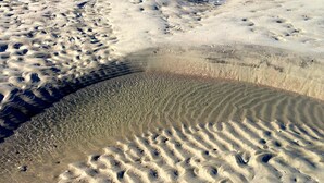 A sandy beach with visible footprints and ripples in the sand, indicating recent activity.