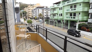 Un balcon agrémenté de meubles en osier, d’une table en verre et offrant une vue sur une rue bordée d’immeubles et de voitures garées.