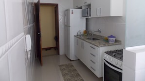 Une cuisine de taille réduite avec des meubles blancs, un four à micro-ondes, un évier et une cuisinière.