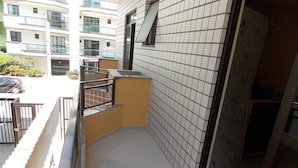 Un petit balcon fermé, doté de murs carrelés et d’une rambarde en métal, qui donne sur un parking et un immeuble à plusieurs étages.