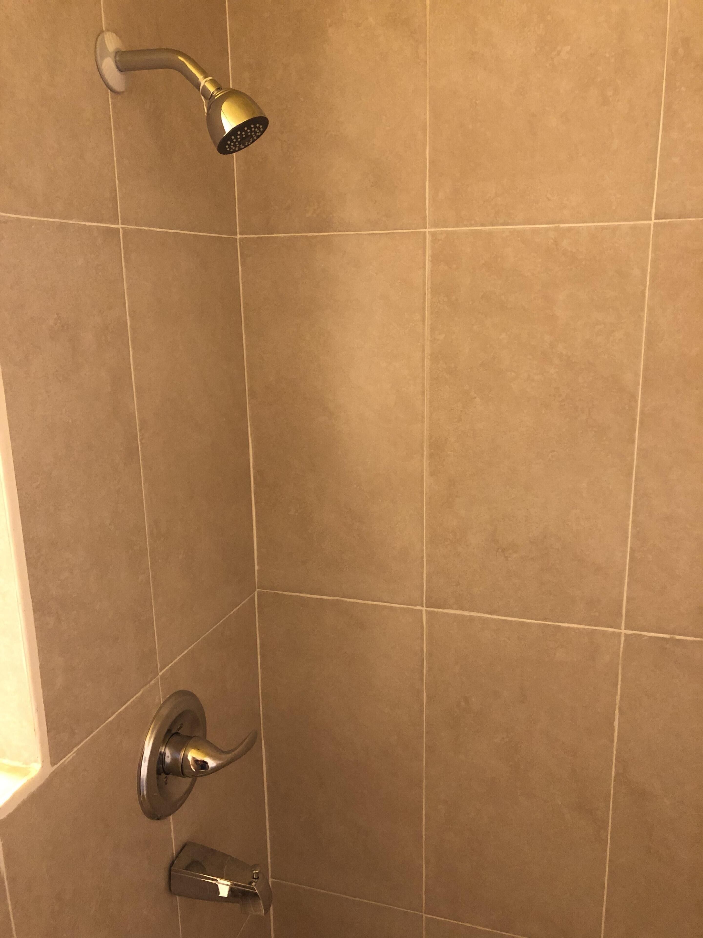 Une douche équipée d’un pommeau de douche à main et d’un robinet de contrôle fixé au mur.