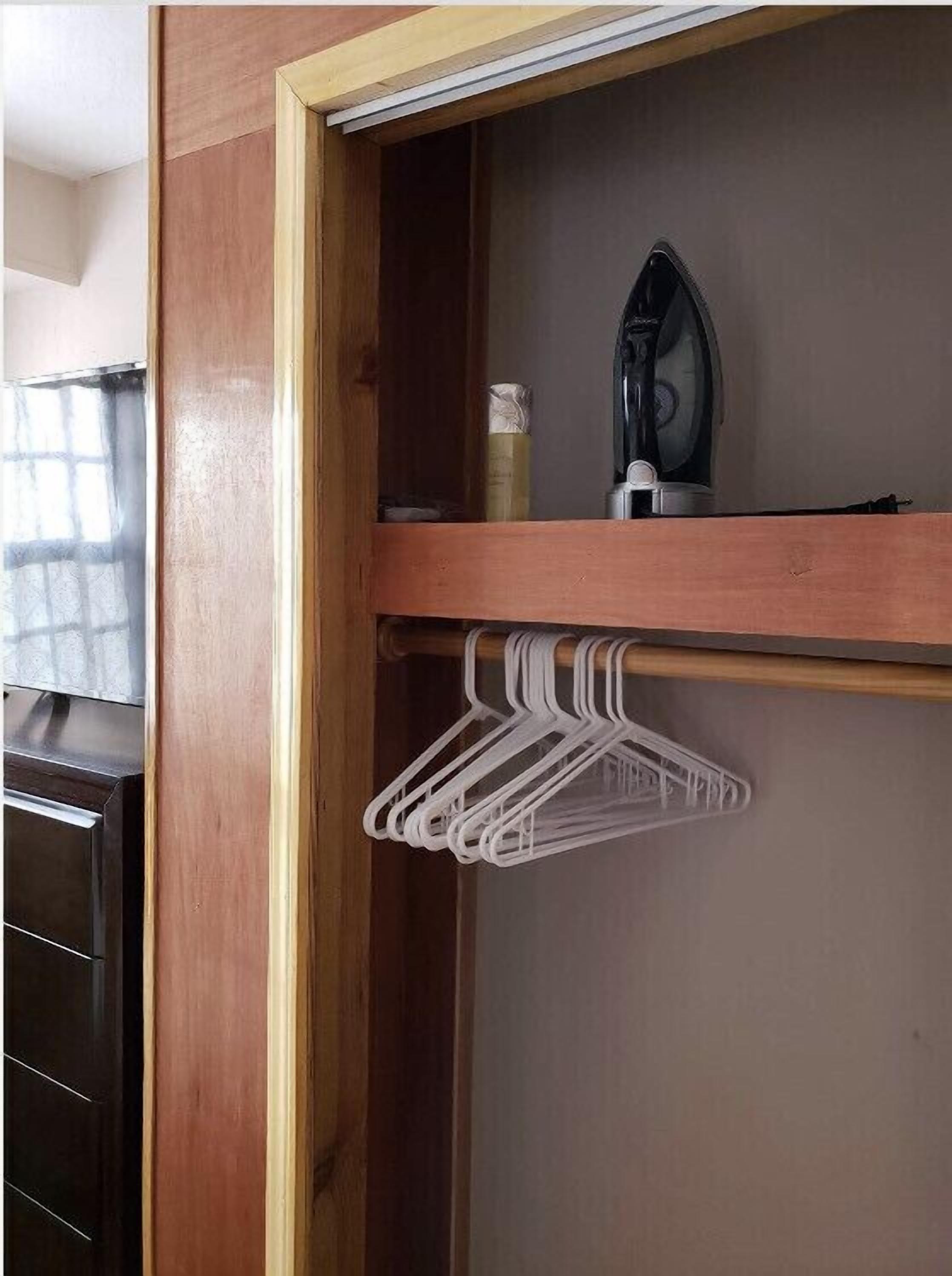 Ein Holzschrank mit Kleiderstange und Bügeleisen auf der Ablagefläche.