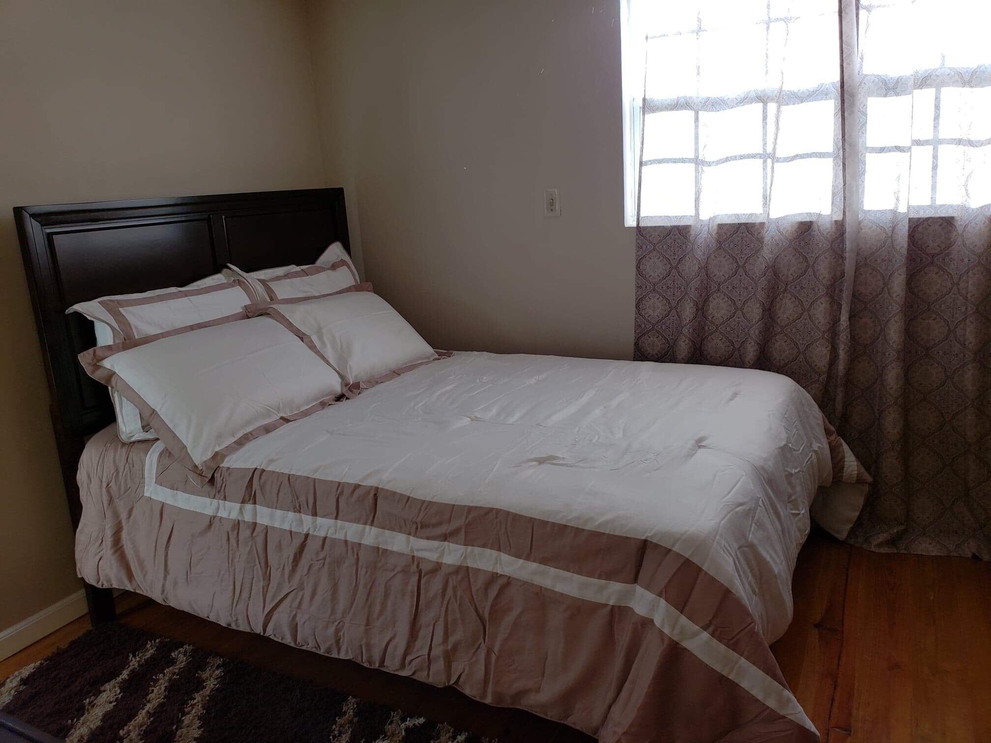 Un dormitorio con cama, ventana con cortinas estampadas y suelo de madera.