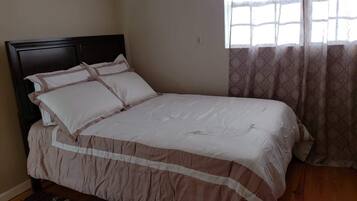 Un dormitorio con cama, ventana con cortinas estampadas y suelo de madera.