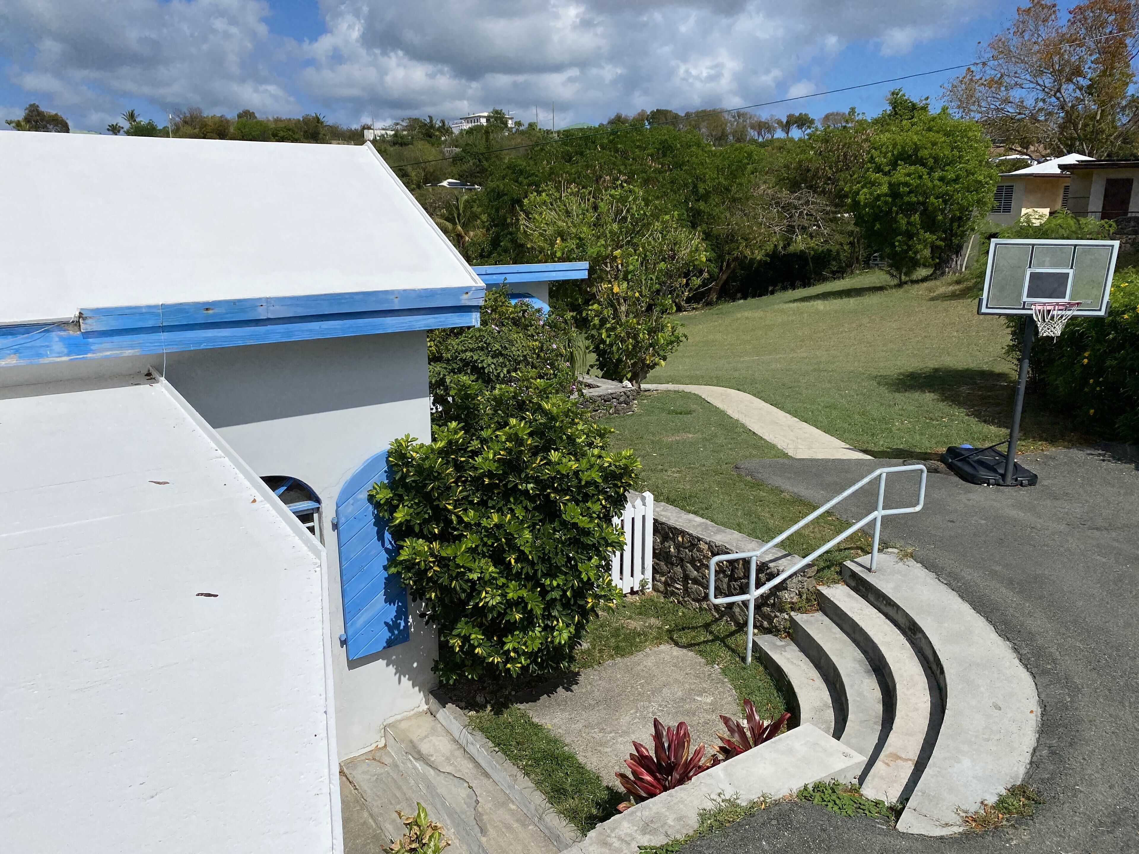 A residential area with a white building, a basketball court, and a staircase leading to a door.