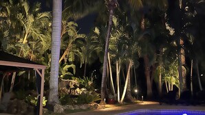A nighttime pool area with palm trees and a covered seating area. - Tropical Retreat Pool Home close to Downtown & Naples Beaches (Naples)