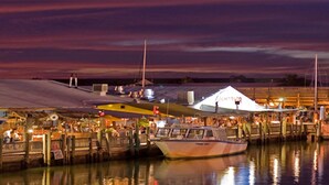 A waterfront marina at dusk with boats docked, a restaurant with outdoor seating, and a large tent structure. - Tropical Retreat Pool Home close to Downtown & Naples Beaches (Naples)