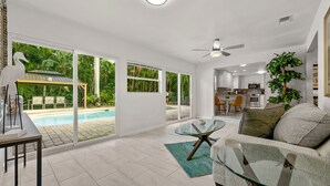 A spacious living room with a glass coffee table, a sofa, and a view of a swimming pool and outdoor seating area. - Tropical Retreat Pool Home close to Downtown & Naples Beaches (Naples)