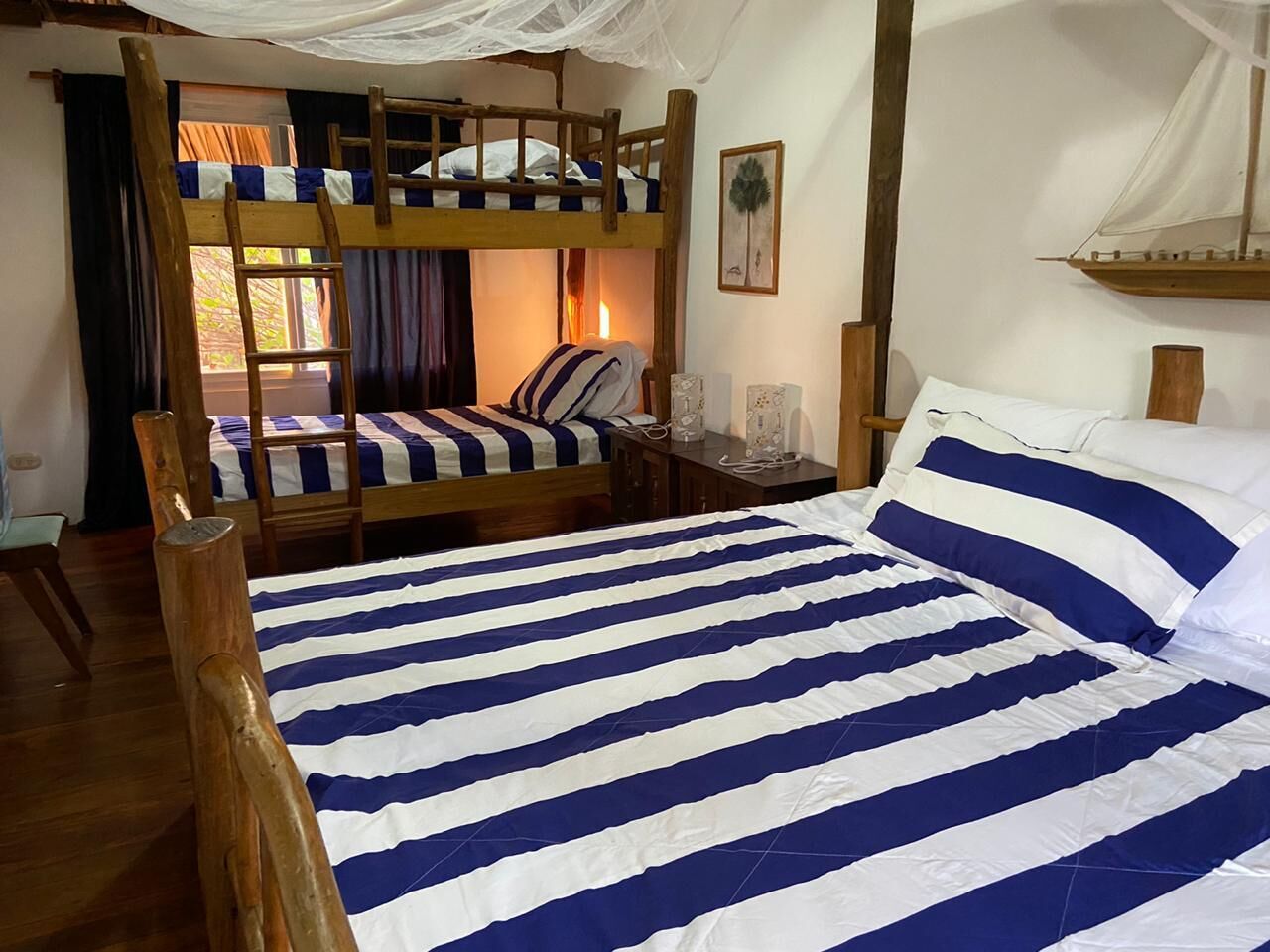 Une chambre avec un lit superposé, un lit simple avec une literie à rayures, des meubles en bois et une petite table avec une lampe.