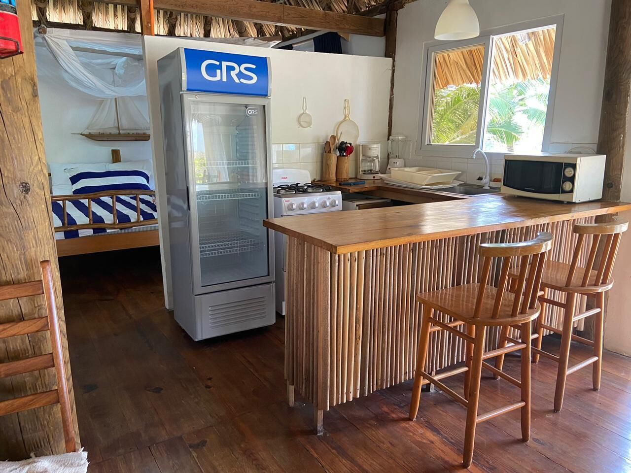 Une cuisine compacte équipée d’un réfrigérateur, d’une cuisinière et d’un four à micro-ondes. On y trouve une table à manger en bois avec des chaises.
