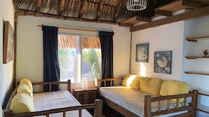 Quarto com duas camas de madeira, janela com cortinas e telhado de palha.