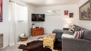 Una sala de estar con un sofá gris, un televisor montado en la pared y un cofre de madera rústica.