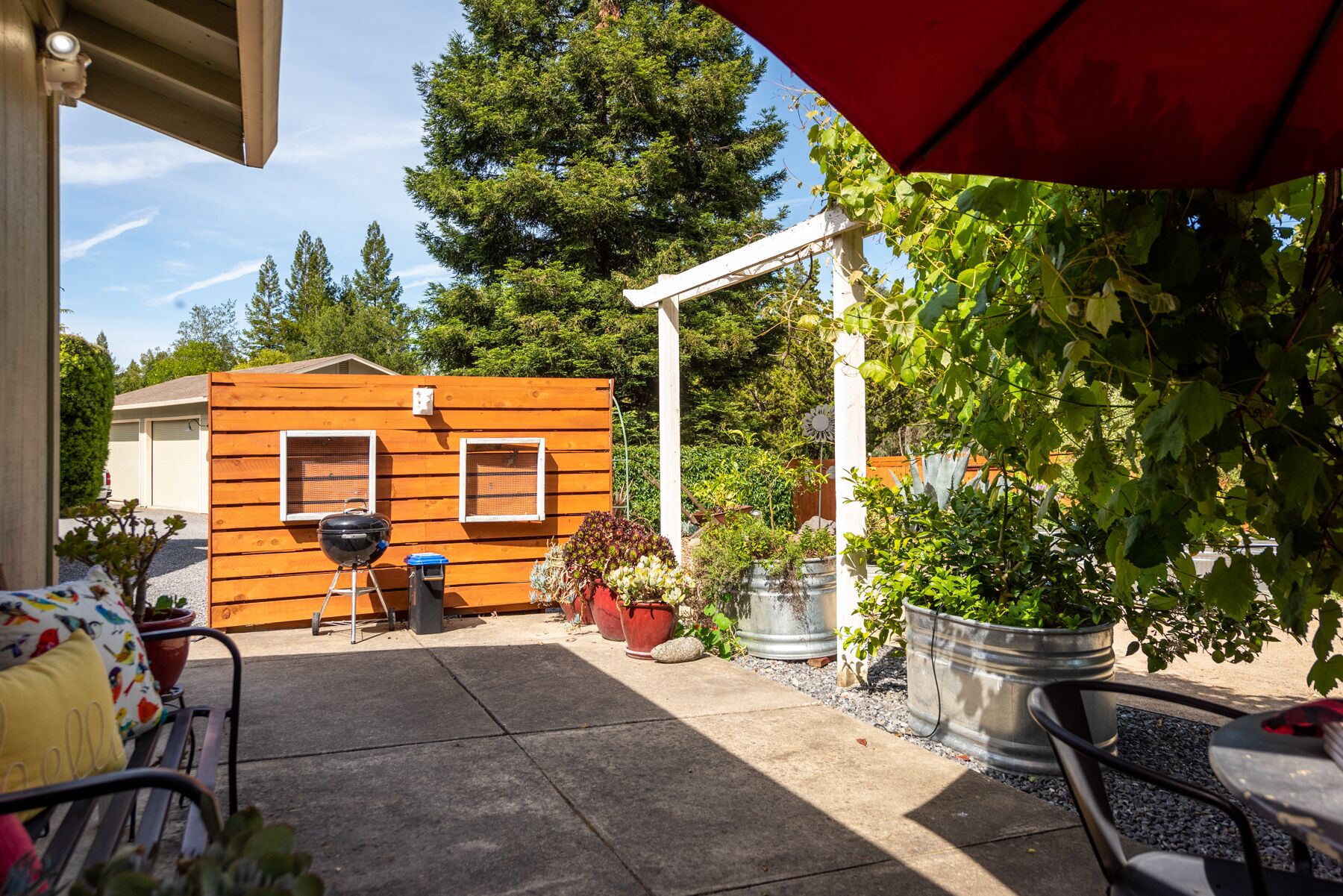 Un patio con una estructura de madera, asientos exteriores y plantas en macetas.
