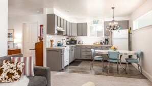 Una cocina moderna con armarios grises, encimera blanca y una zona de comedor con una mesa redonda y sillas azules.