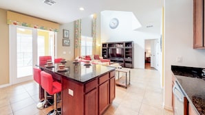 A spacious kitchen with a central island, red bar stools, and a dining area with a sofa.