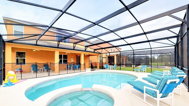 A covered swimming pool with lounge chairs and a hot tub, surrounded by a glass enclosure.
